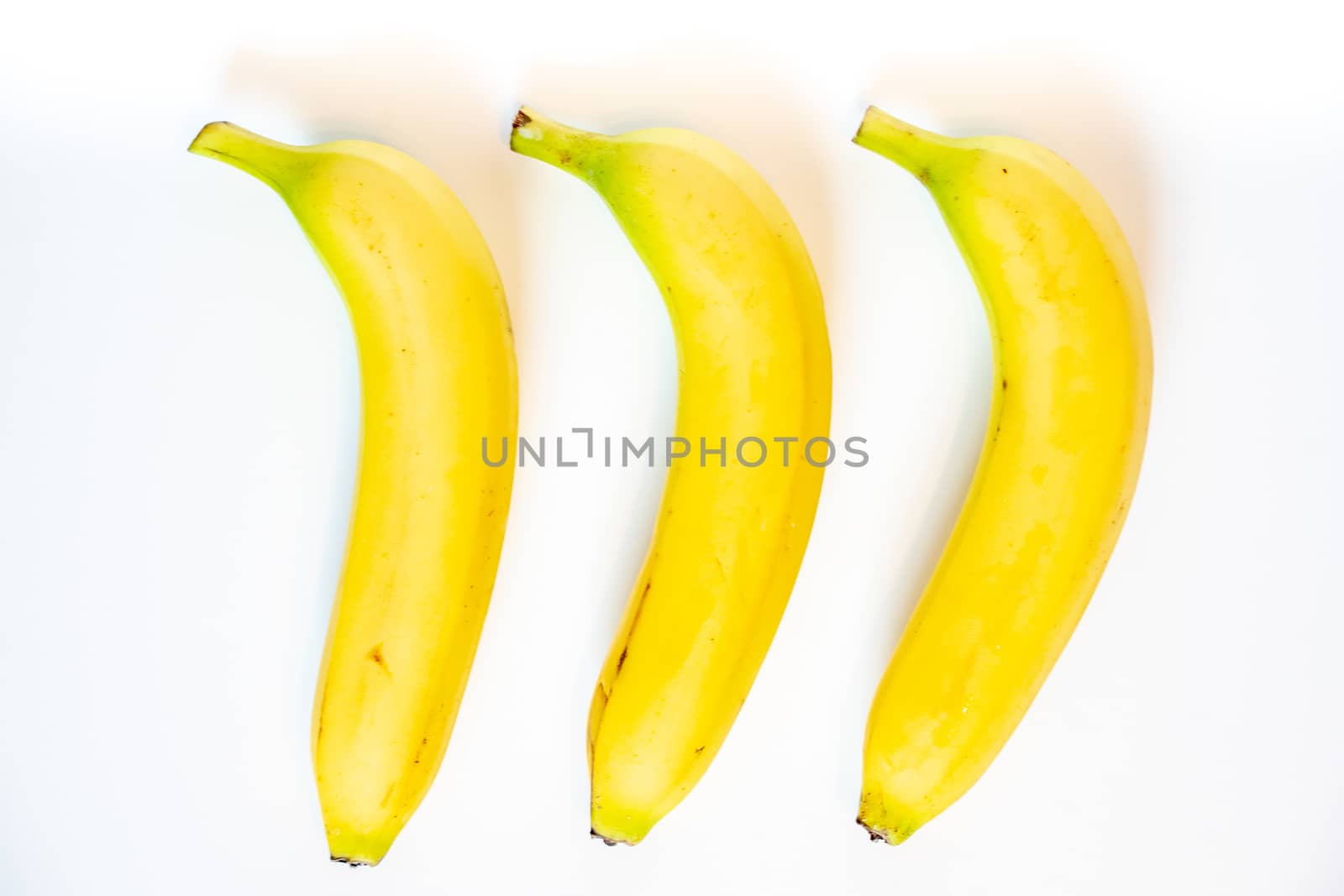 Three whole bananas laid in a row against a plain whit background