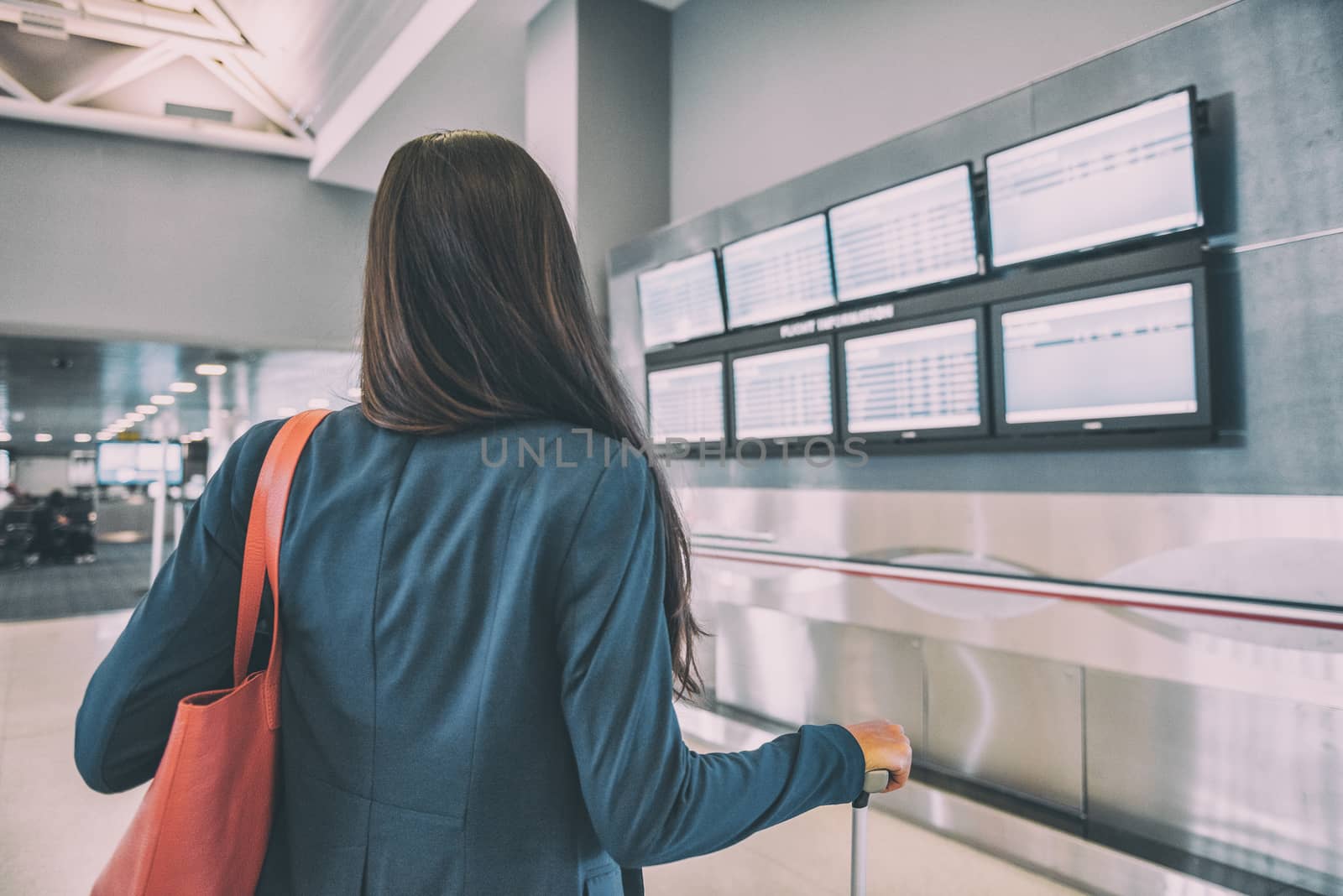 Travel airport tourist woman waiting for delayed flight looking at airport terminal screens showing cancelled flights, corona virus COVID-19 concept. Vacation cancellation from tourism industry.