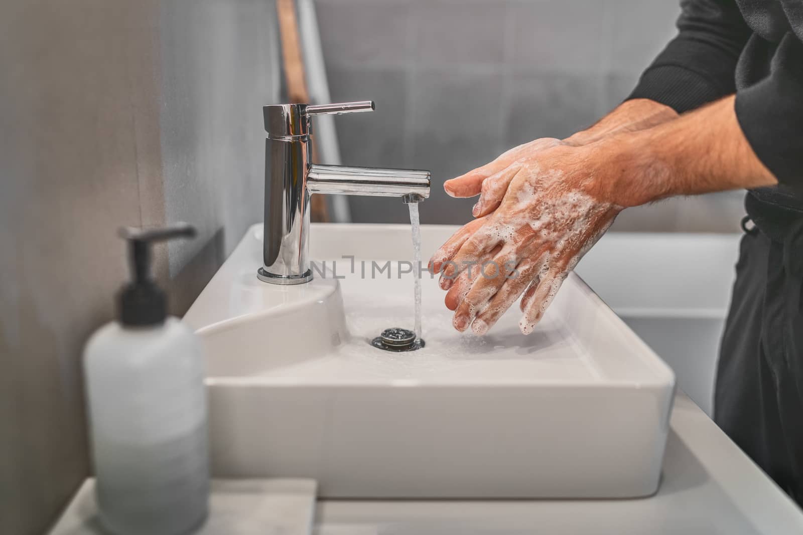 Washing hands with soap and hot water at home bathroom sink man cleansing hand hygiene for coronavirus outbreak prevention. Corona Virus pandemic protection by washing hands frequently.