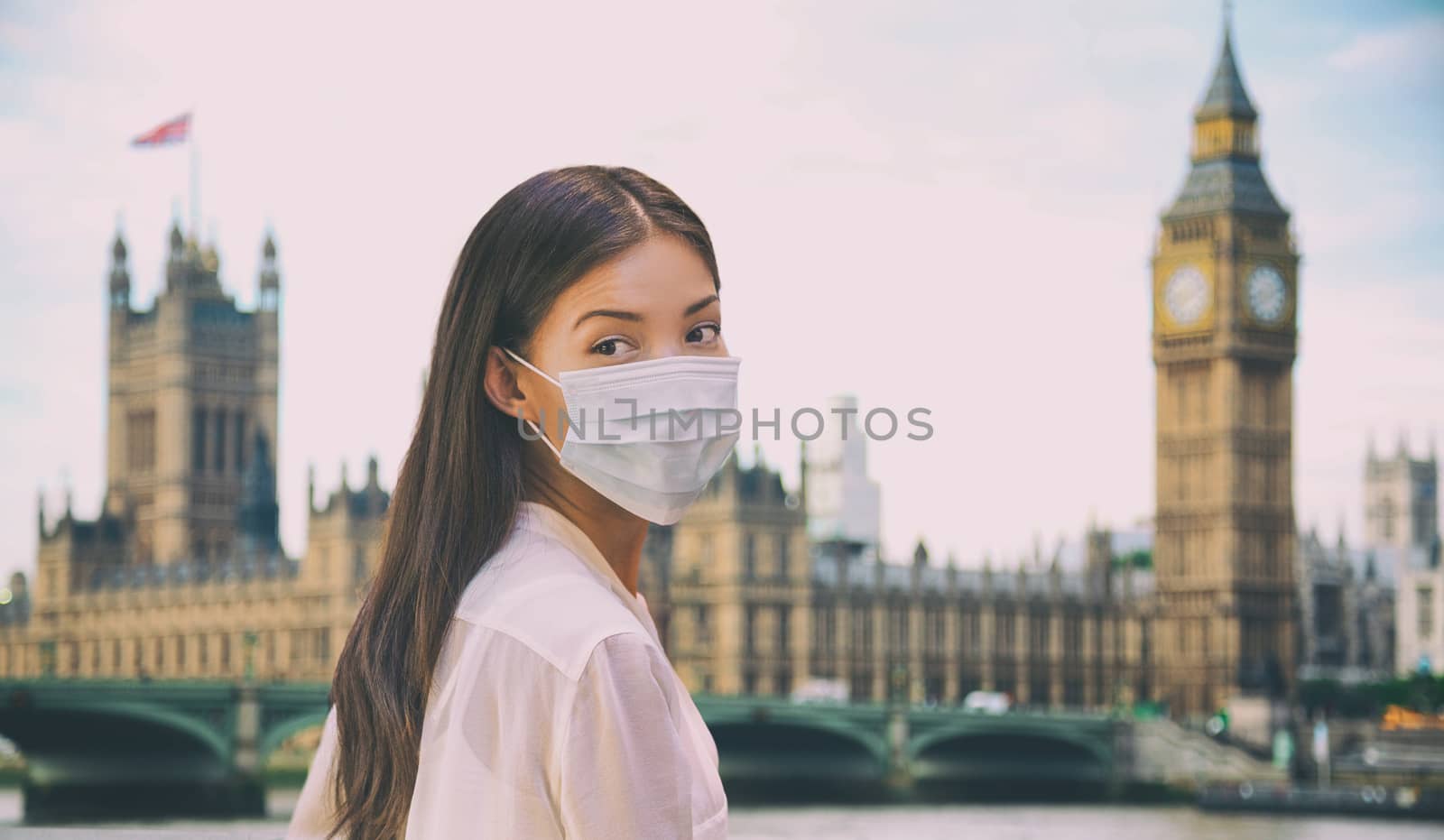 Corona virus travel corona virus spread prevention asian woman tourist wearing protective face mask on UK London city sightseeing holiday vacation. Famous british landmark background panoramic.