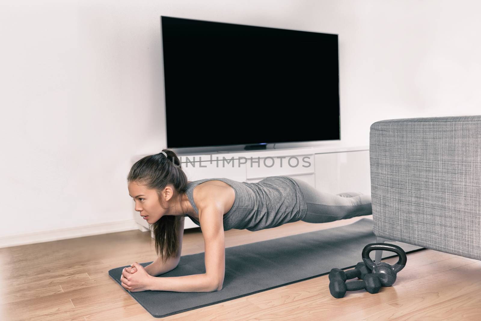 Fitness workout at home indoors. Asian girl doing plank exercises to exercise core watching tv videos of fit class. Young woman training muscles in front of the TV without going to the gym by Maridav