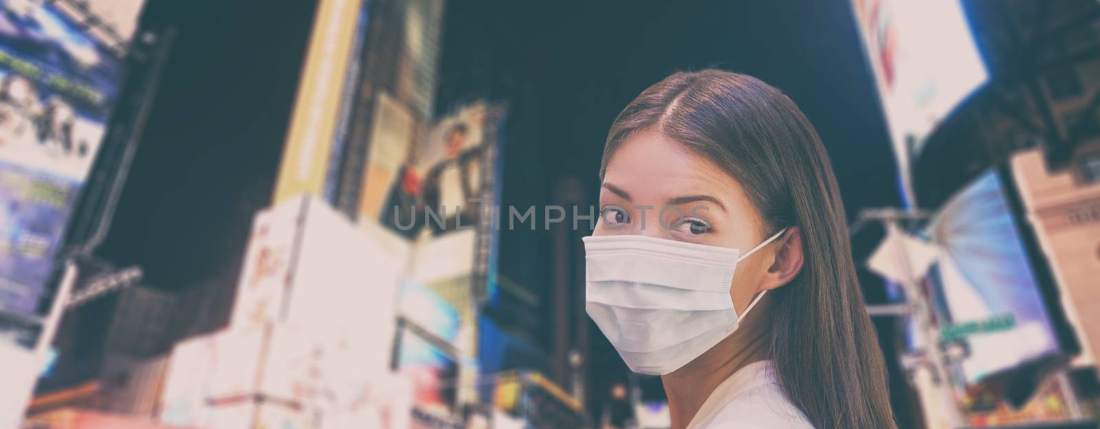 Corona virus NYC travel ban China woman tourist walking in New York city street wearing protective mask for coronavirus pandemic. Panoramic banner background of night skyline by Maridav