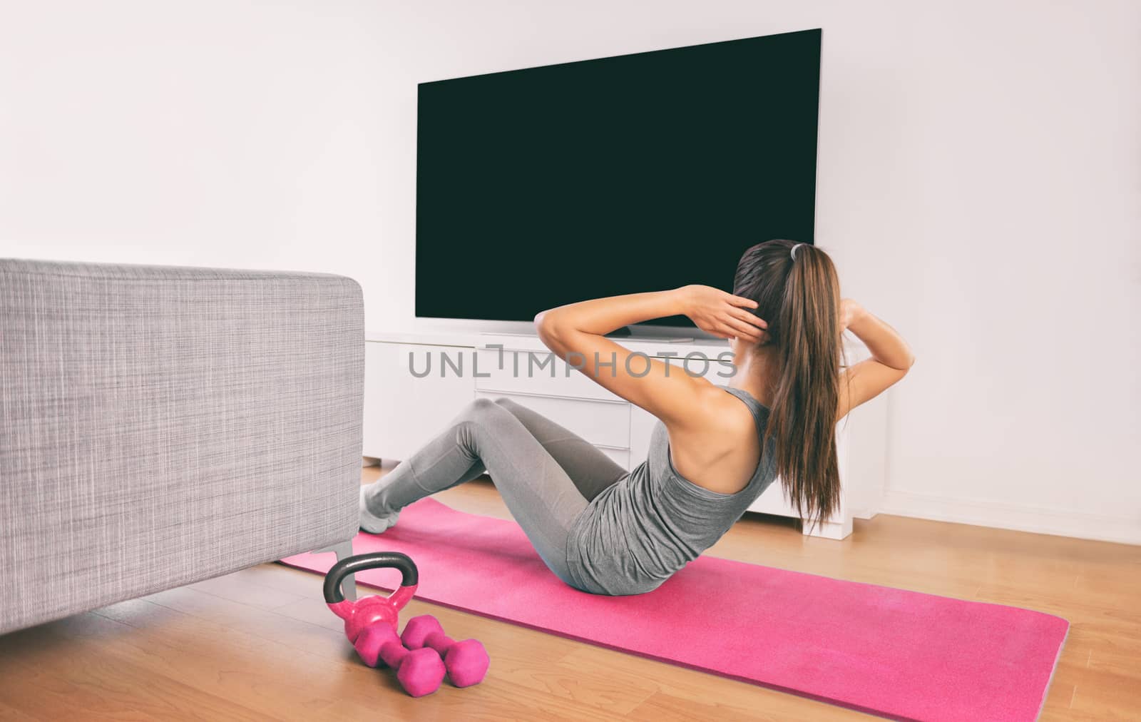 Home fitness woman doing strength training abs situps bodyweight floor exercises watching online livestream workout, web videos casted on smart tv in living room of house or apartment.