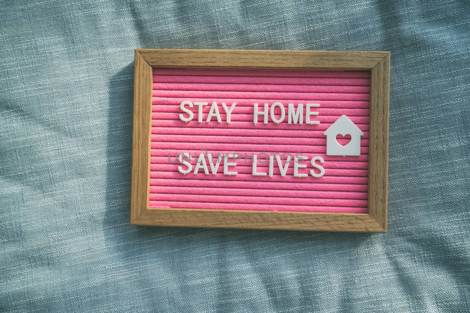 Coronavirus quote stay home, save lives pink felt board sign with message of self isolation for social responsability on home sofa background. COVID-19 text to promote staying at home by Maridav