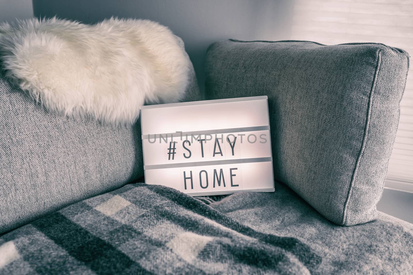 Coronavirus home lightbox sign with hashtag message Hashtag STAYHOME glowing on home sofa with cozy lambswool fur, blanket. COVID-19 text to promote self isolation staying at home by Maridav