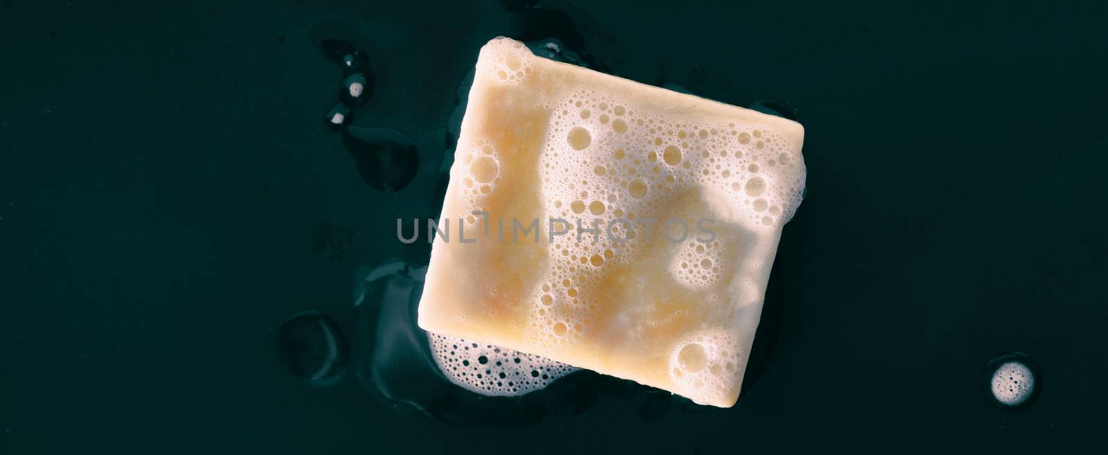 Bar of soap with foam bubbles on black background panoramic banner texture. Top view by Maridav