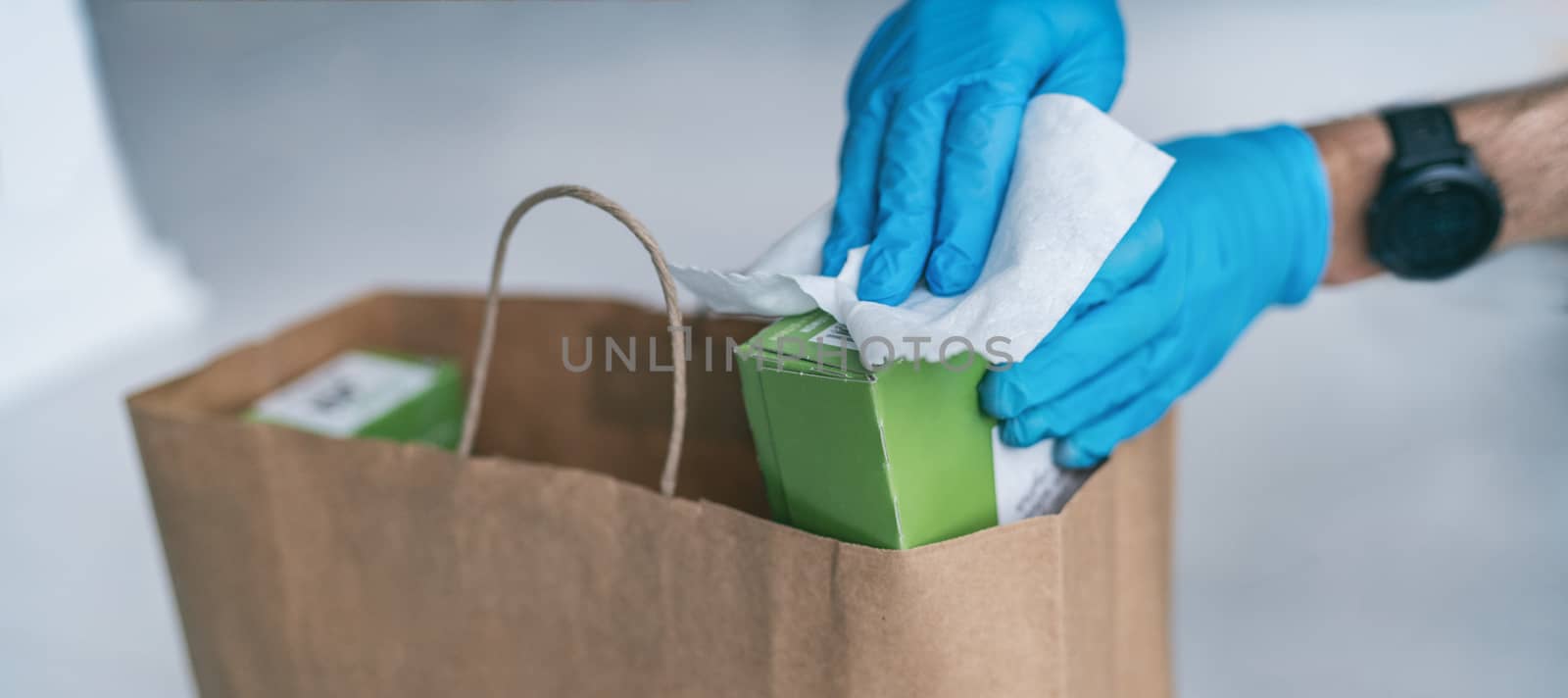 Coronavirus wiping down grocery packages after receiving home delivery wearing gloves, using disinfecting sanitizing wipes to wipe the surfaces clean. Cleaning of COVID-19 virus.