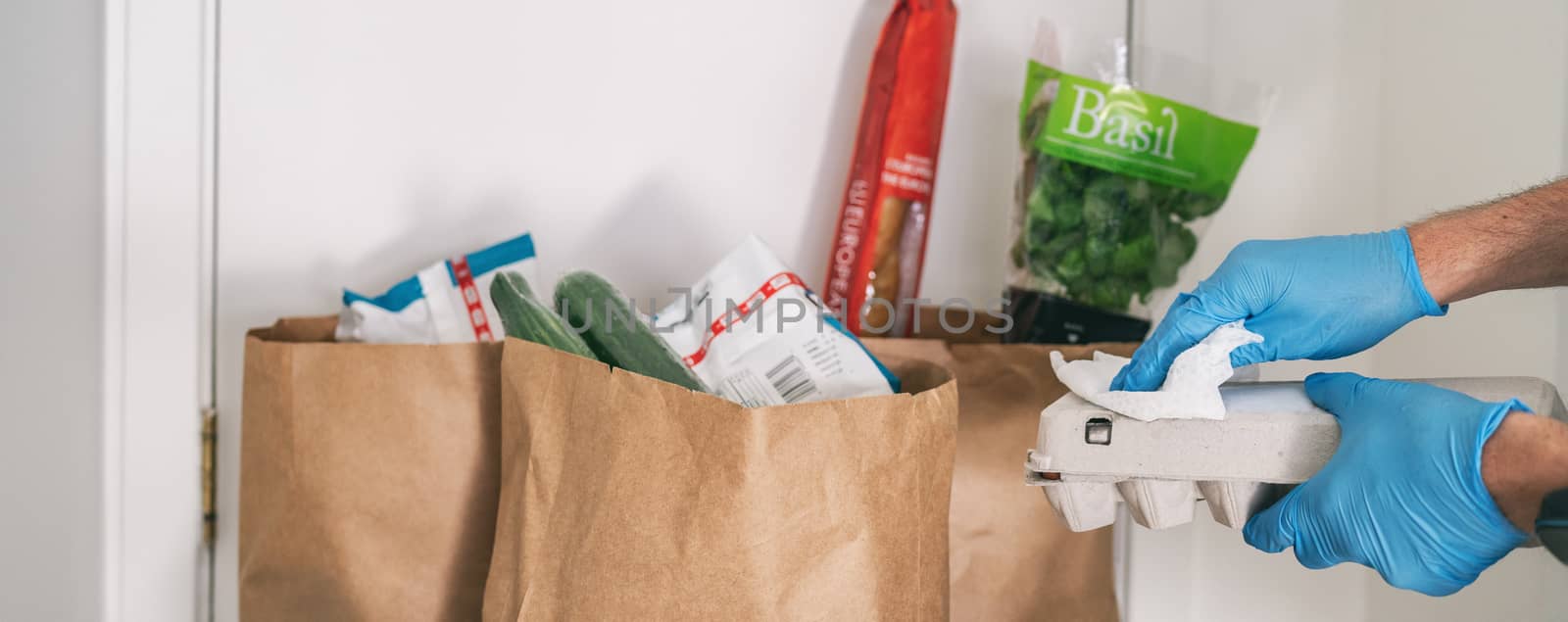 Cleaning groceries with disinfecting wipes as coronavirus prevention. Man wiping down grocery packages after receiving home delivery wearing gloves to wipe the surfaces clean. Cleaning of COVID-19.