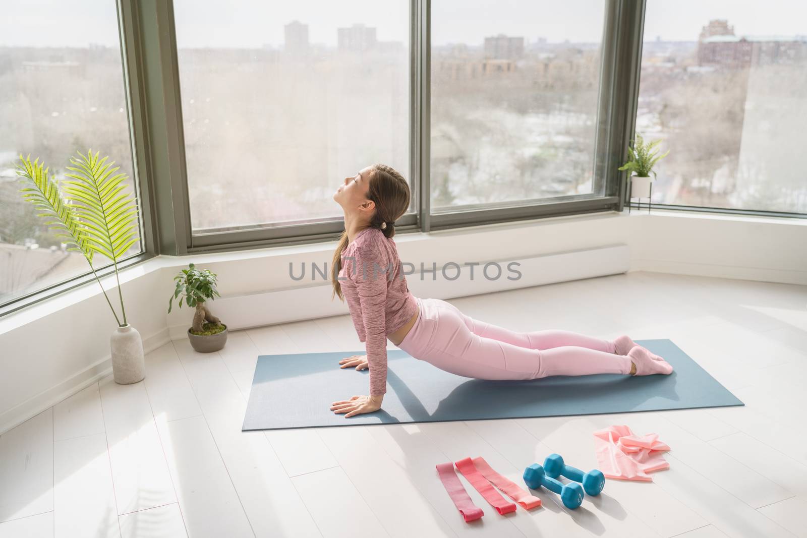 Home yoga workout woman exercising at home stretching legs doing sun salutation cobra pose. Fitness at home girl working out in morning sunlight in living room of apartment.