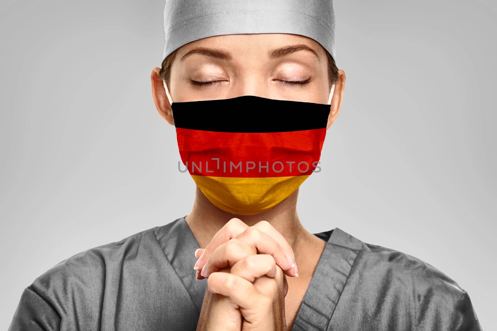 German doctor praying for help with Germany flag on surgical mask. Young woman medical needing PPE help to fight COVID-19 Coronavirus .