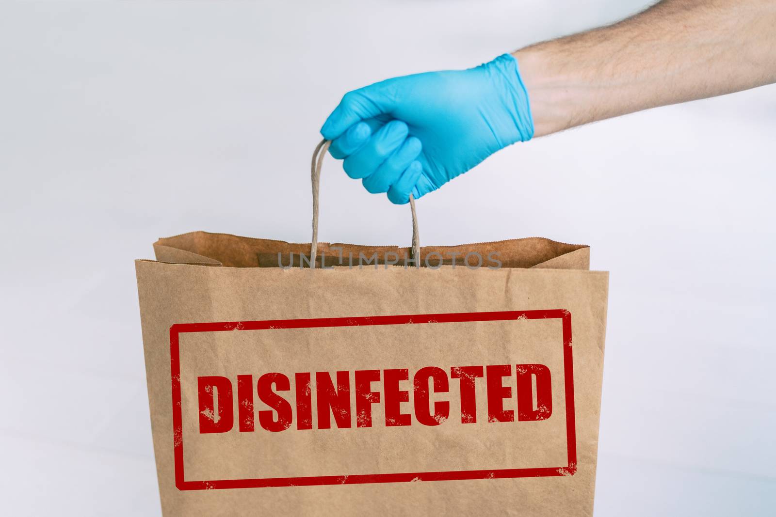 Delivery bag to home from online grocery shopping with stamp of safety DISIFINFECTED written on the paper side. Man holding groceries with medical blue glove.