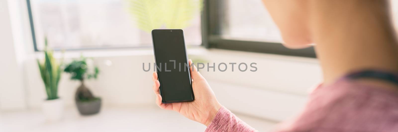 Woman using mobile phone staying home watching videos online on 5g data app view from behind holding black empty screen panoramic banner lifestyle by Maridav
