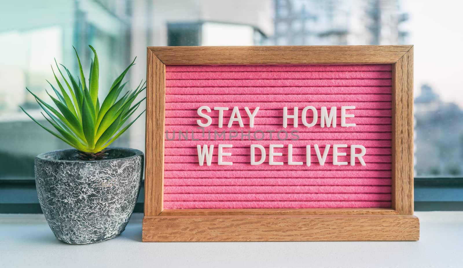 COVID-19 STAY HOME WE DELIVER Coronavirus social distancing restaurant business message sign with text offering online delivery to home, staying inside. Pink felt board with plant.