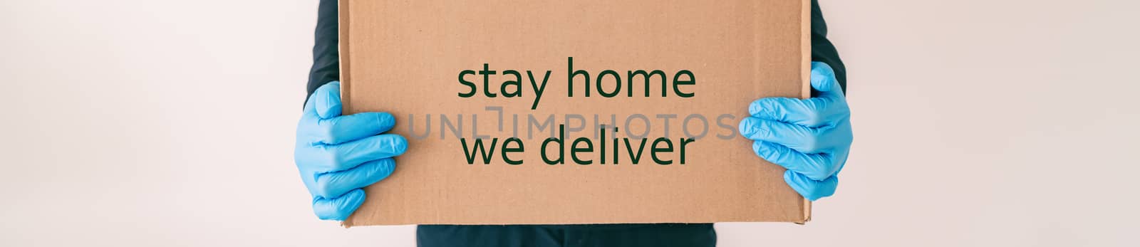 Home delivery with quote STAY HOME WE DELIVER on cardboard box banner. Food grocery delivered with gloves for COVID-19 quarantine from coronavirus social distancing. man giving purchase.