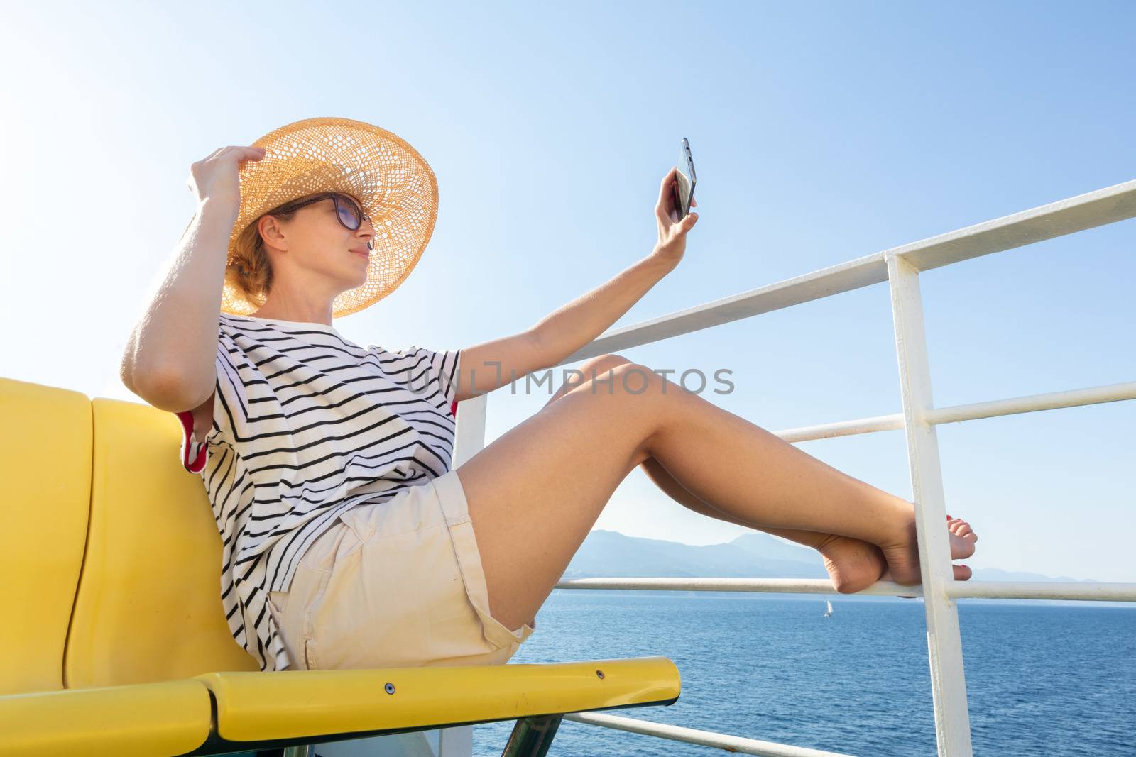 Beautiful, romantic blonde woman taking selfie self portrait on summer vacations traveling by cruse ship ferry boat. Summer vacation lifestyle.