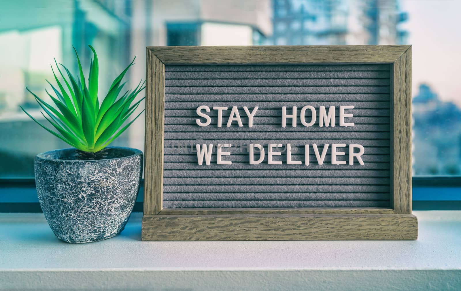 STAY HOME WE DELIVER Coronavirus social distancing restaurant business message sign. COVID-19 online delivery to home, staying inside. Grey felt board with plant.