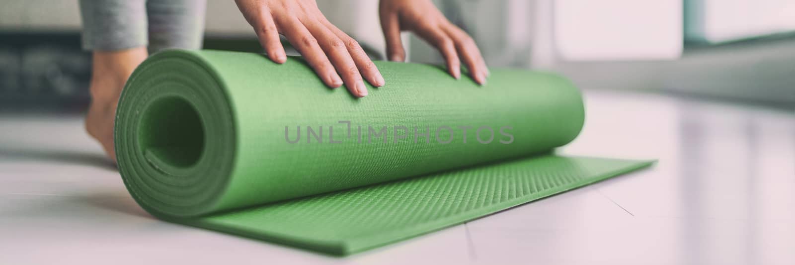 Home meditation woman rolling yoga exercise mat in living room for pilates workout online class banner panoramic apartment lifestyle.