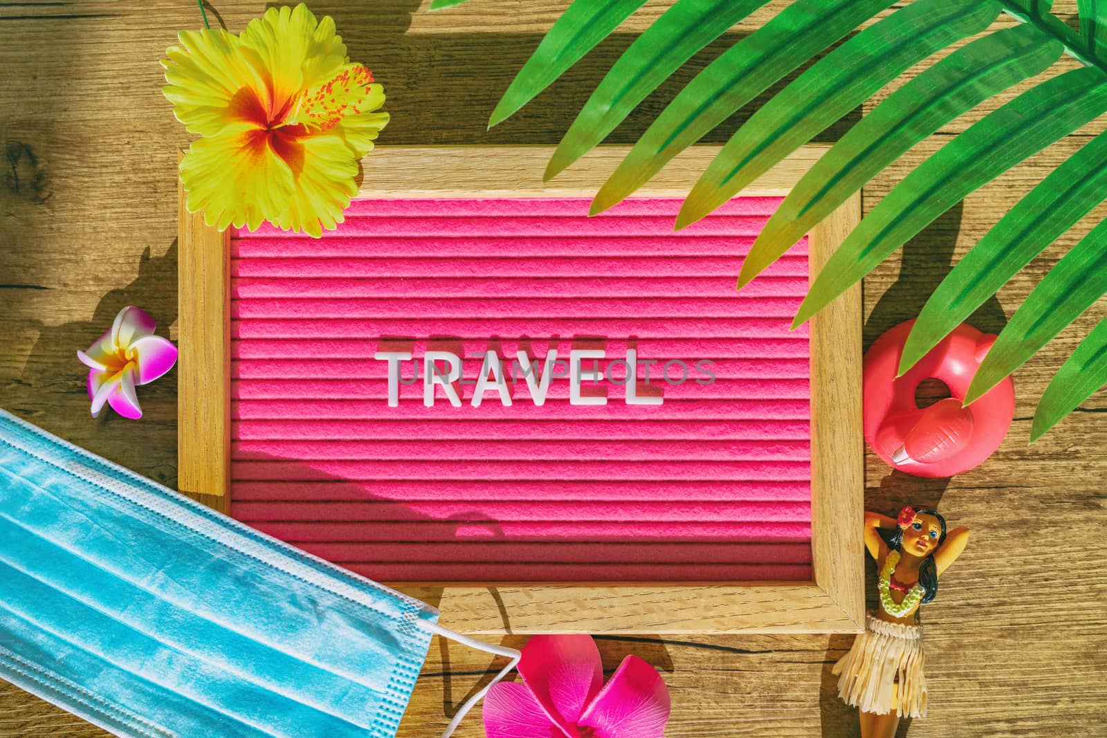 TRAVEL tropical sign with medical face mask for new reality after coronavirus pandemic. Funny pink felt board with text and flowers, hula doll, surgical mandatory wearing.