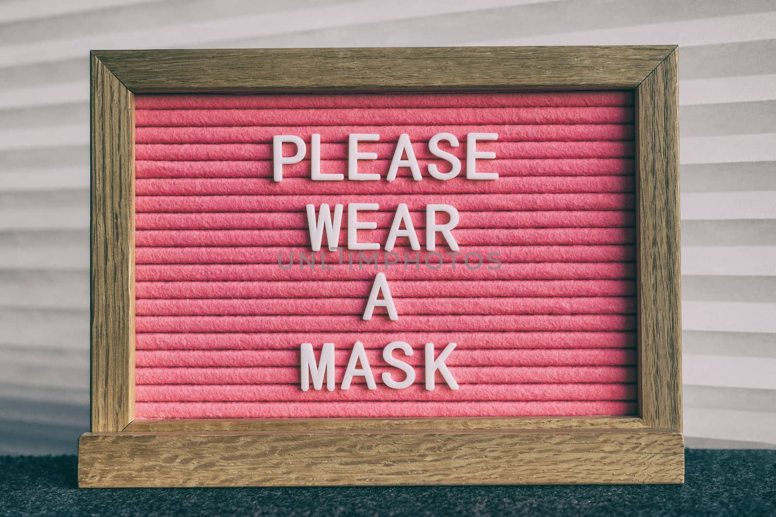COVID-19 sign PLEASE WEAR A MASK at grocery store entrance for coronavirus prevention. Message on pink felt letter board. Compulsory measure in businesses for face protection wearing.