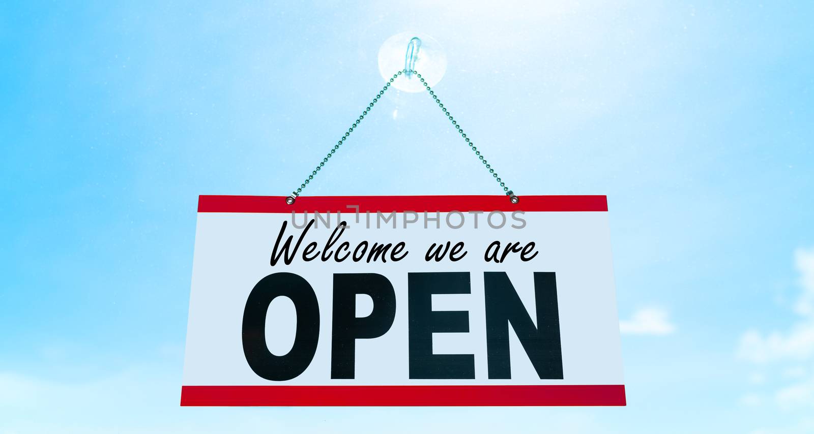 COVID-19 Open business sign saying Welcome we are OPEN hanging on window storefront reopening Retail businesses opening again. Sun blue sky summer background. end of confinement by Maridav