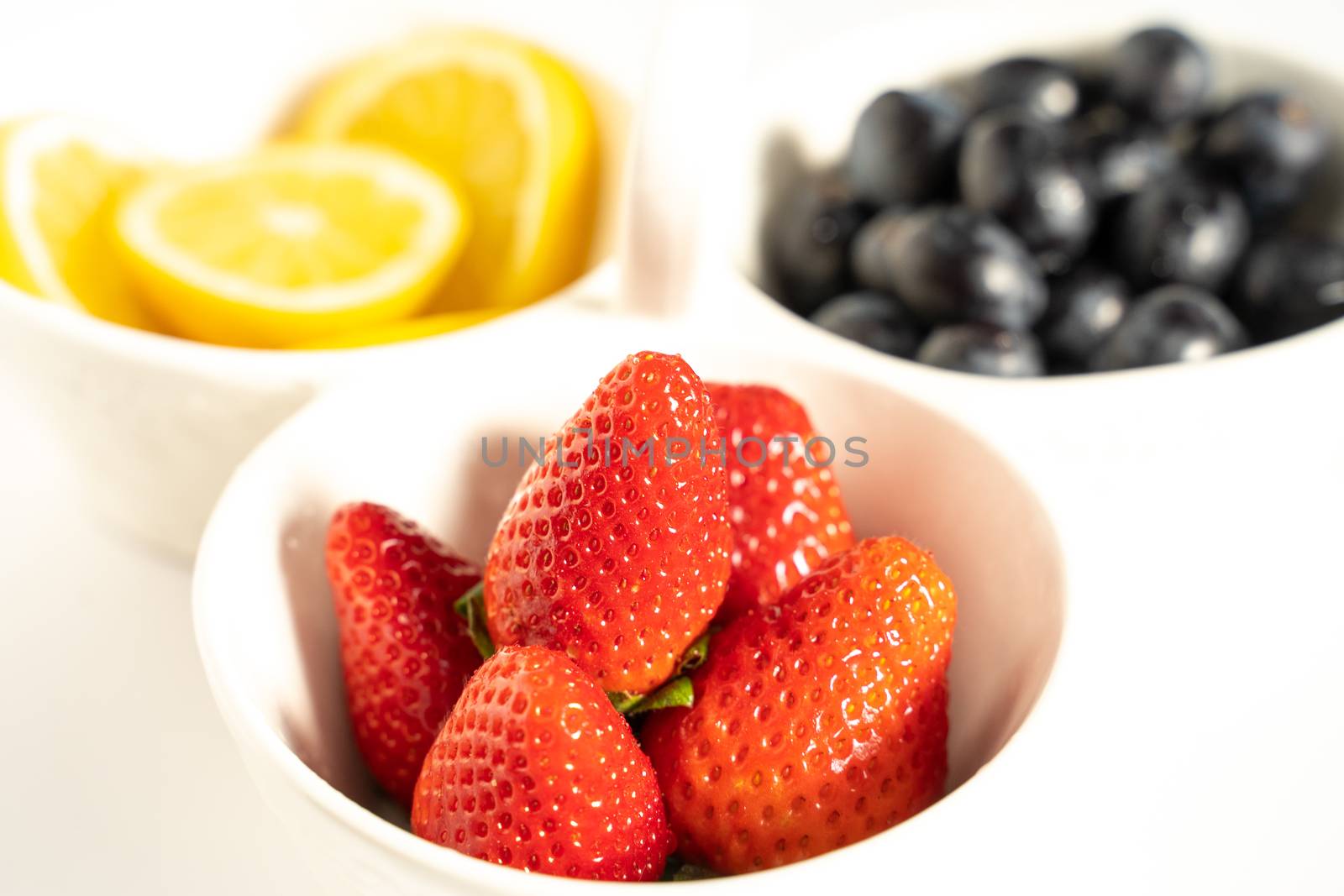 A serving dish filled with strawberries, lemon slices and black grapes against a plain white background