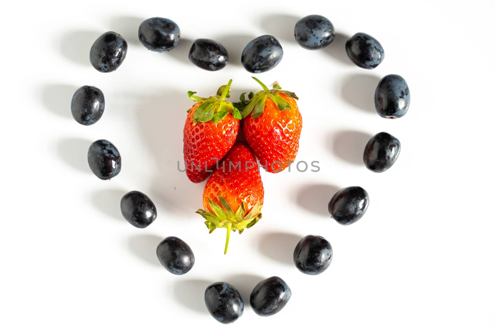 Three strawberries in the center of a heart shape pattern of black grapes