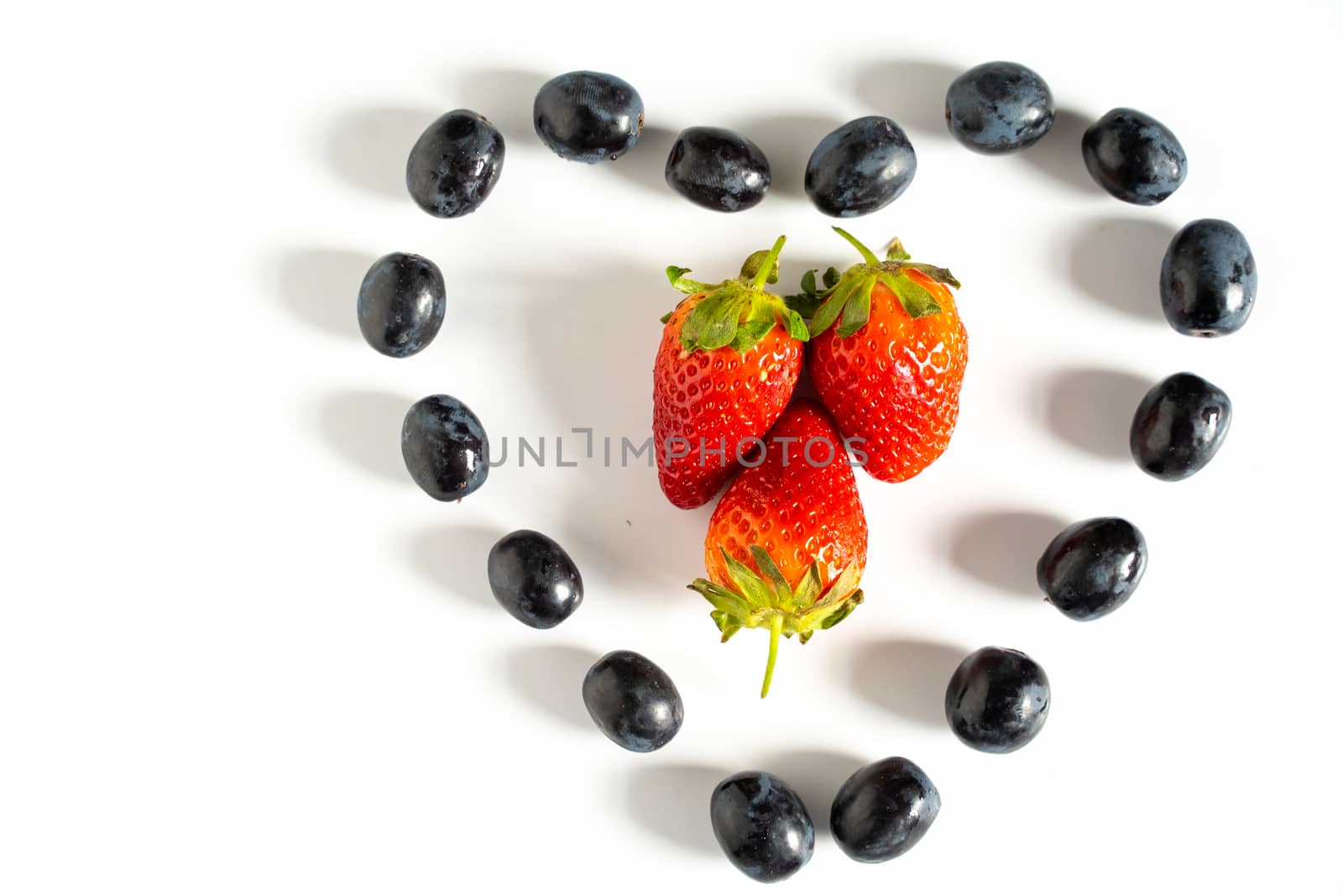 Three strawberries in the center of a heart shape pattern of black grapes