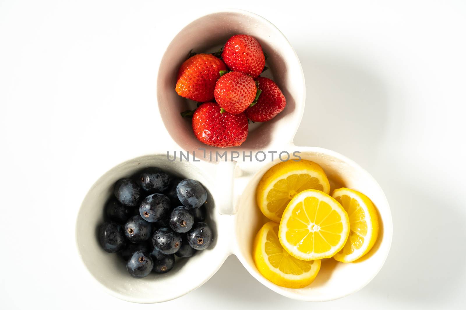 A serving dish filled with strawberries, lemon slices and black grapes against a plain white background