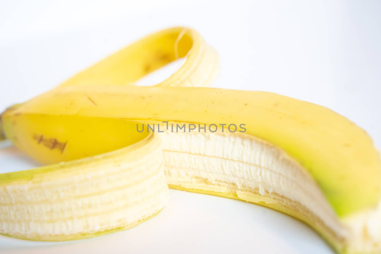 A Whole banana with the skin peeled back against a plain white background