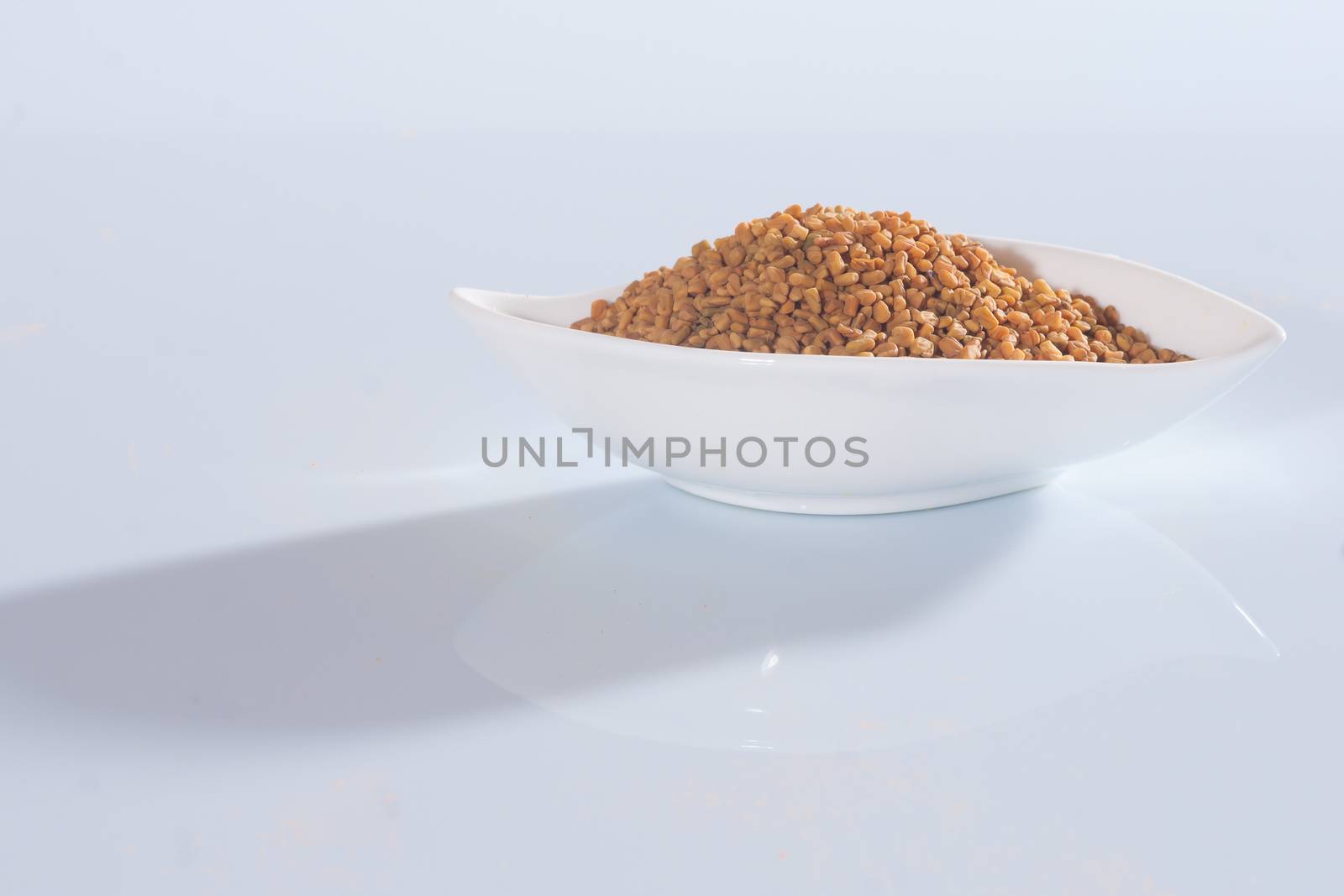 Fenugreek seeds in a white bowl on white background