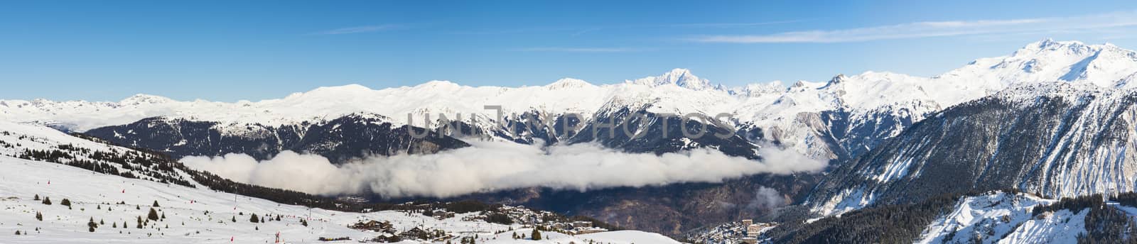 Panoramic view down snow covered valley in alpine mountain range with coniferous pine trees and clouds