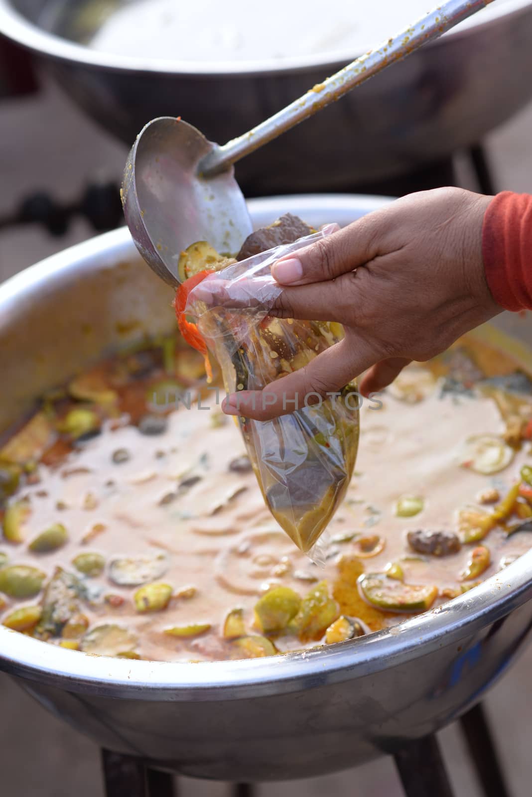 Woman hand holding dipper scooping green curry with chicken Put in a plastic bag And there was a basin with curry on a blurred background.