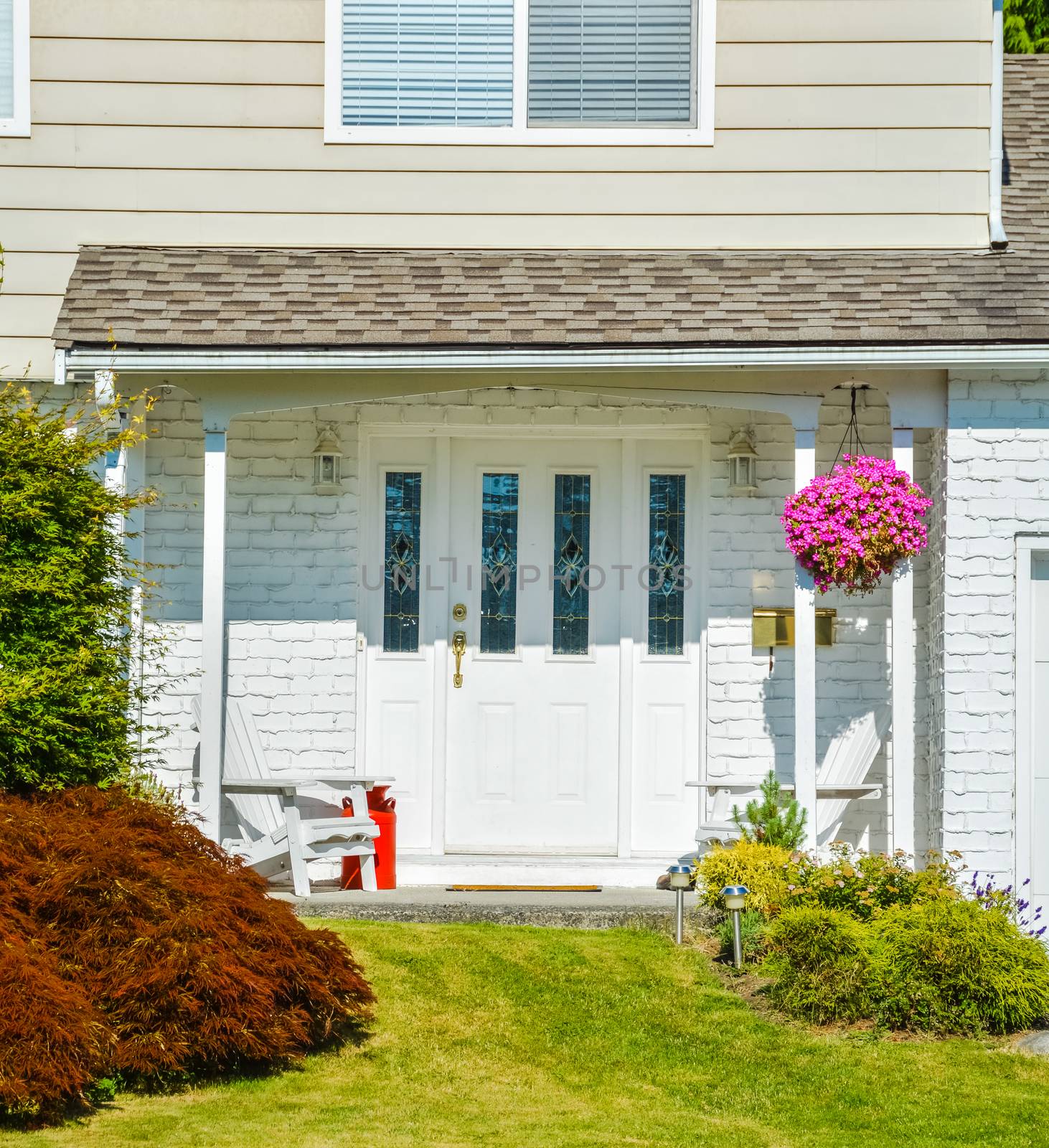 Entrance of residential house decorated with backet of flowers, two white chairs and red churn