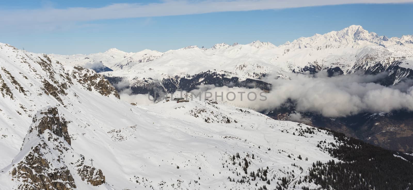Aerial high angle panoramic view down snow covered valley in alpine mountain range with cumulus clouds