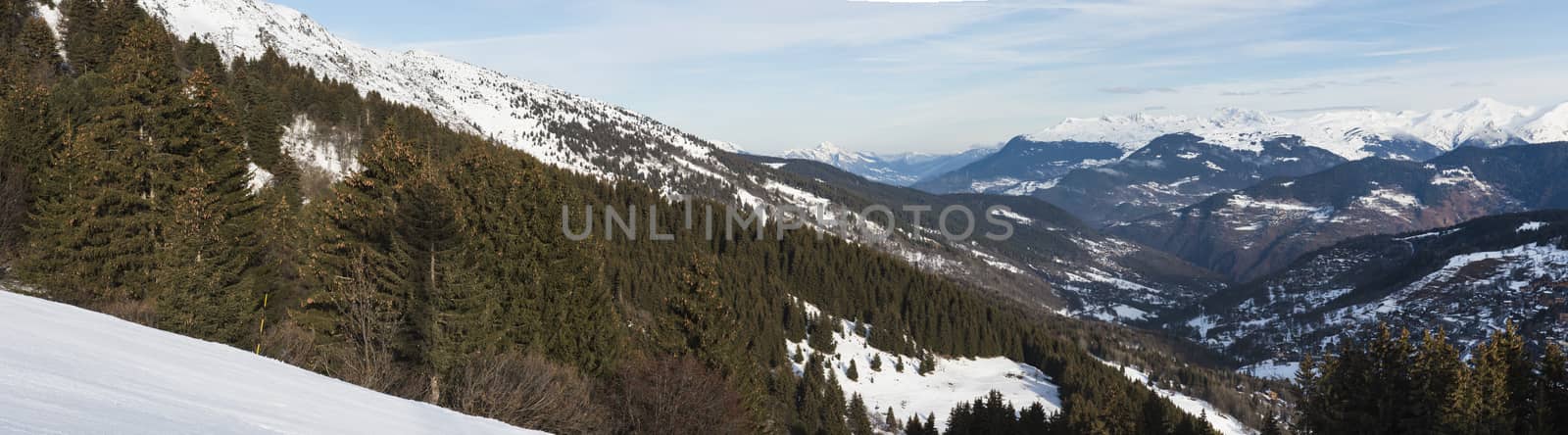 Panoramic view down snow covered valley in alpine mountain range with conifer pine trees