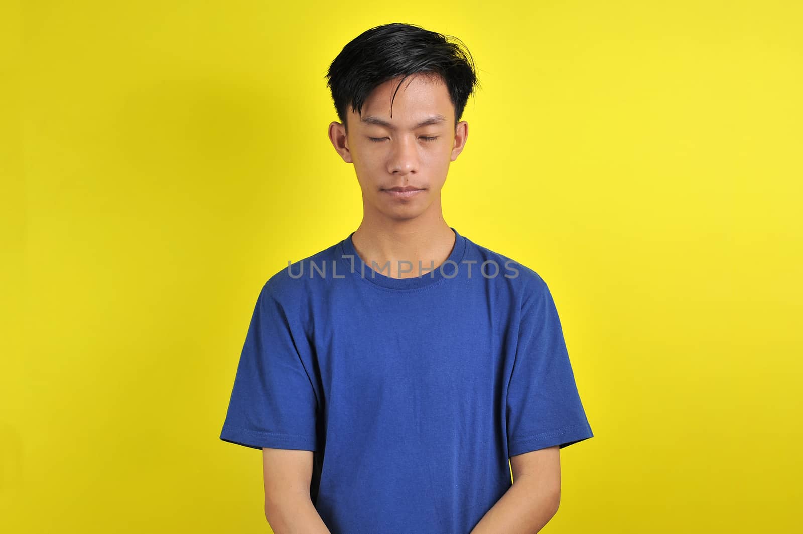 Portrait of young Asian man close his eyes, isolated on yellow background
