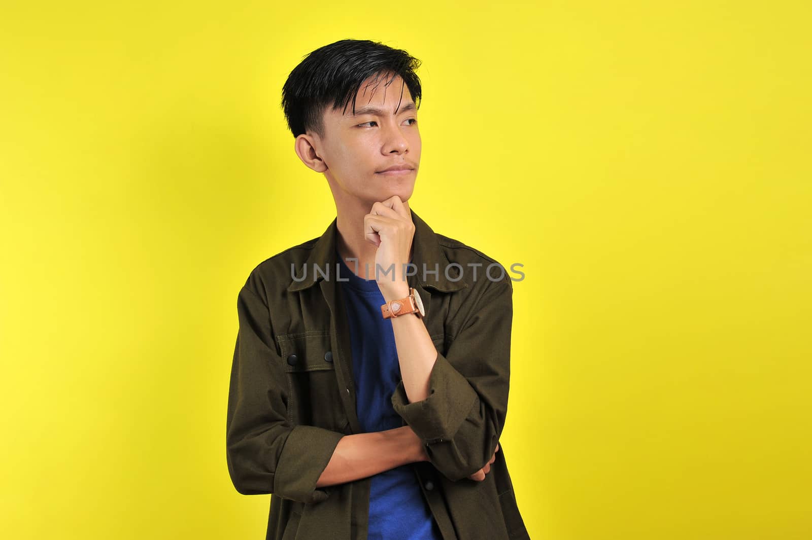 Handsome young Asian man looking at copy space or blank area, isolated on yellow background