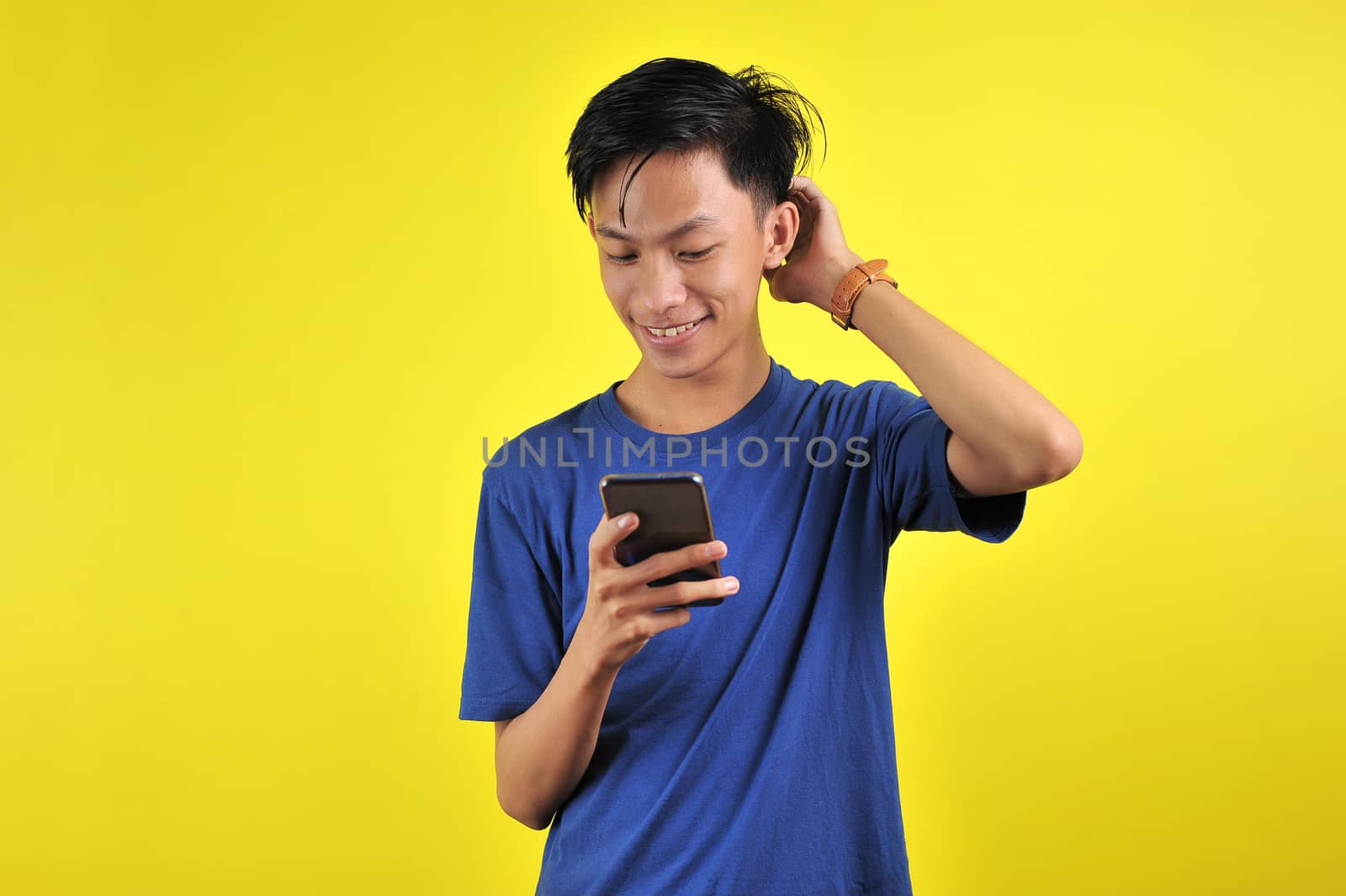 Happy of young good looking Asian man smiling using smartphone isolated on yellow background