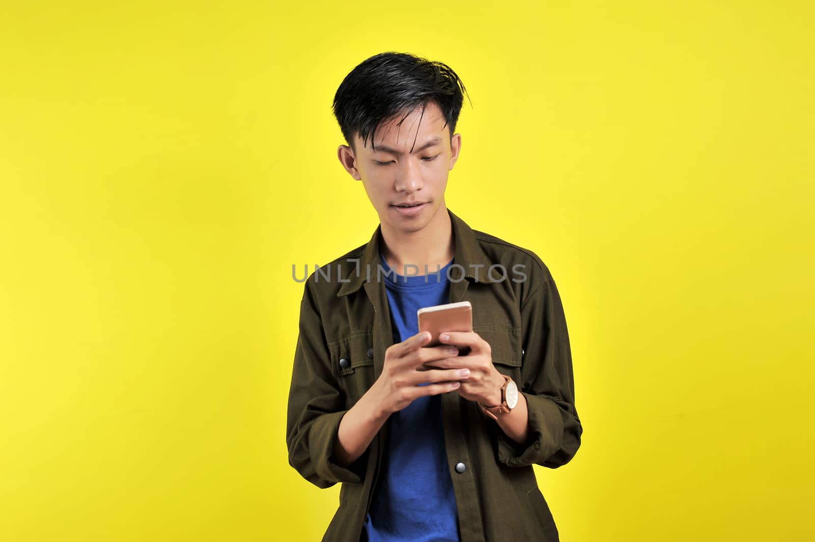 Shocked face of Asian man in white shirt looking at phone screen, isolated on yellow background.