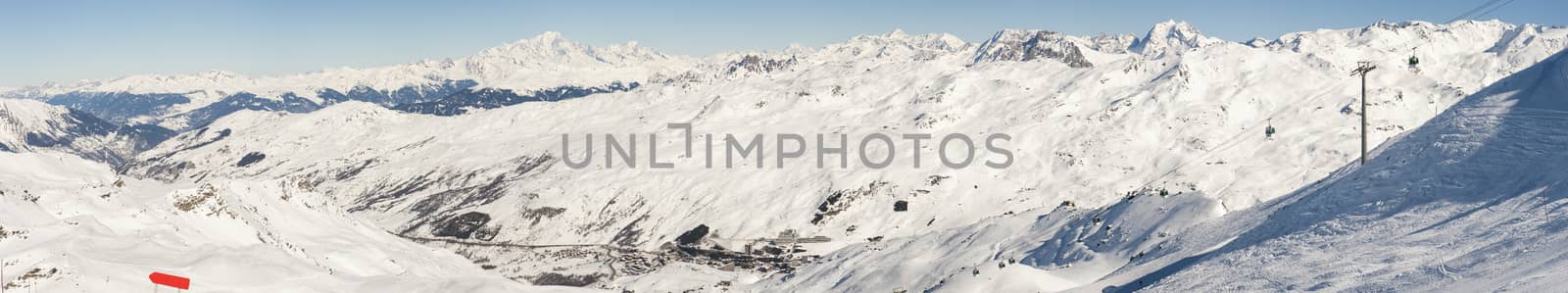 View down a snowy piste in alpine mountain valley with ski resort village