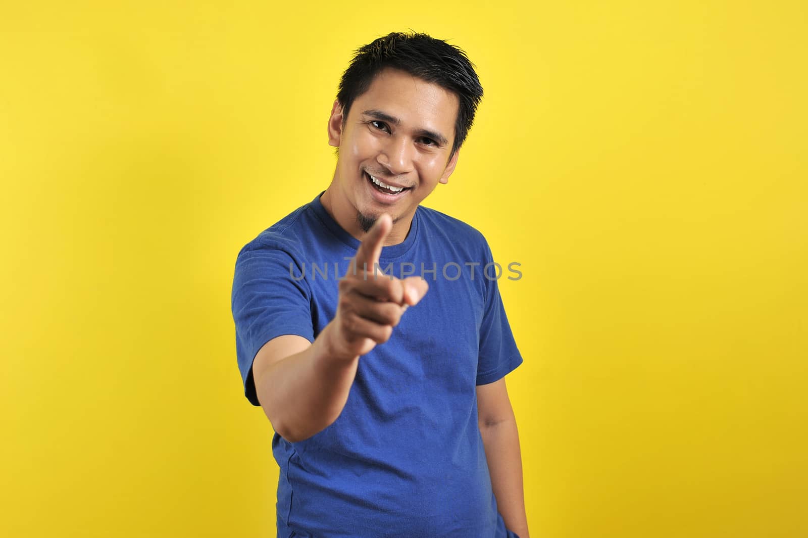 Happy young Asian man smiling pointing to the camera, isolated on yellow