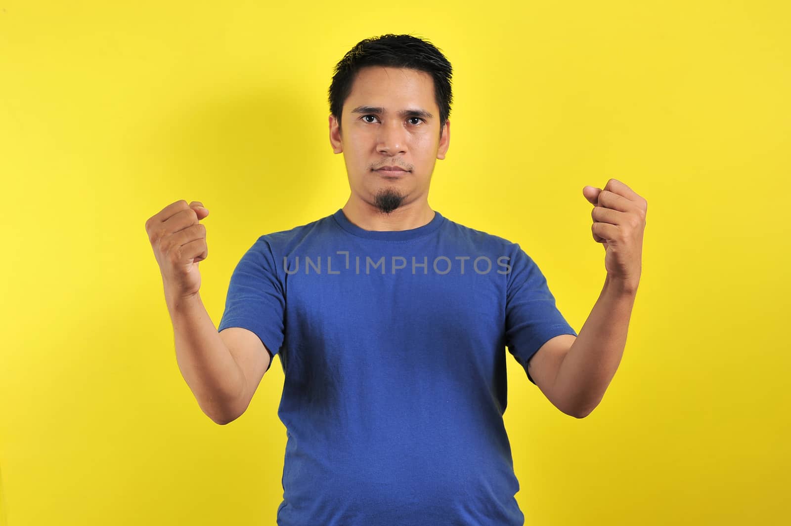 Handsome young Asian man showing muscle, strong gesture and showing power, isolated on orange background