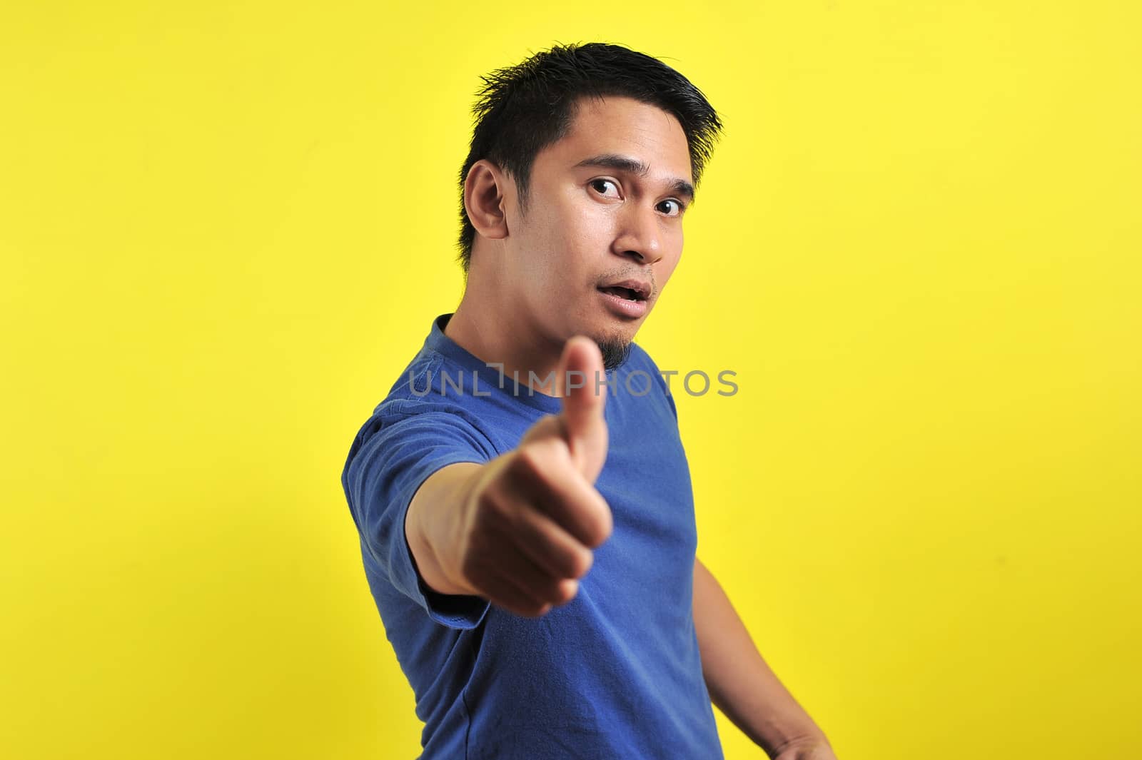 Portrait of young Asian man laughing with showing thumbs up at camera, isolated on yellow