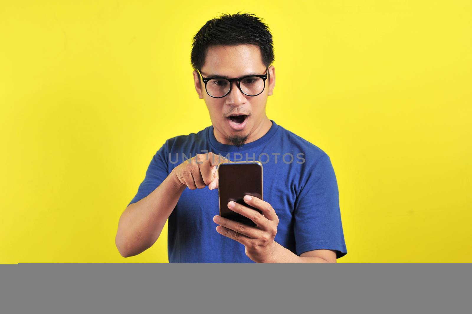 Shocked face of Asian man in blue shirt looking at phone screen  by heruan1507