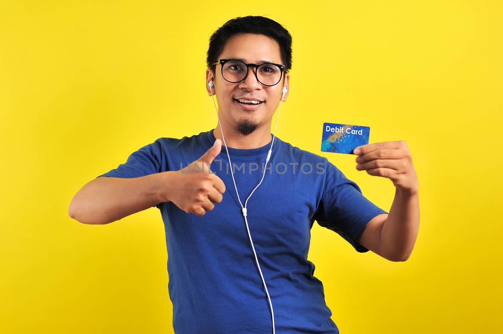 Young Asian man love his debit card, isolated on yellow background