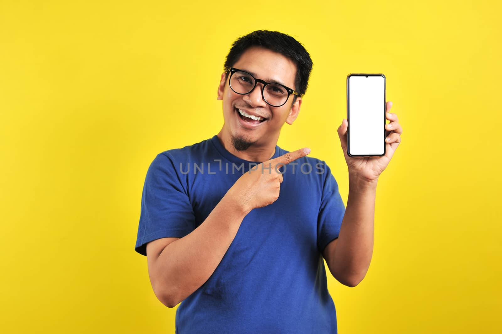 Happy Asian man showing a phone screen and pointing, isolated on yellow background