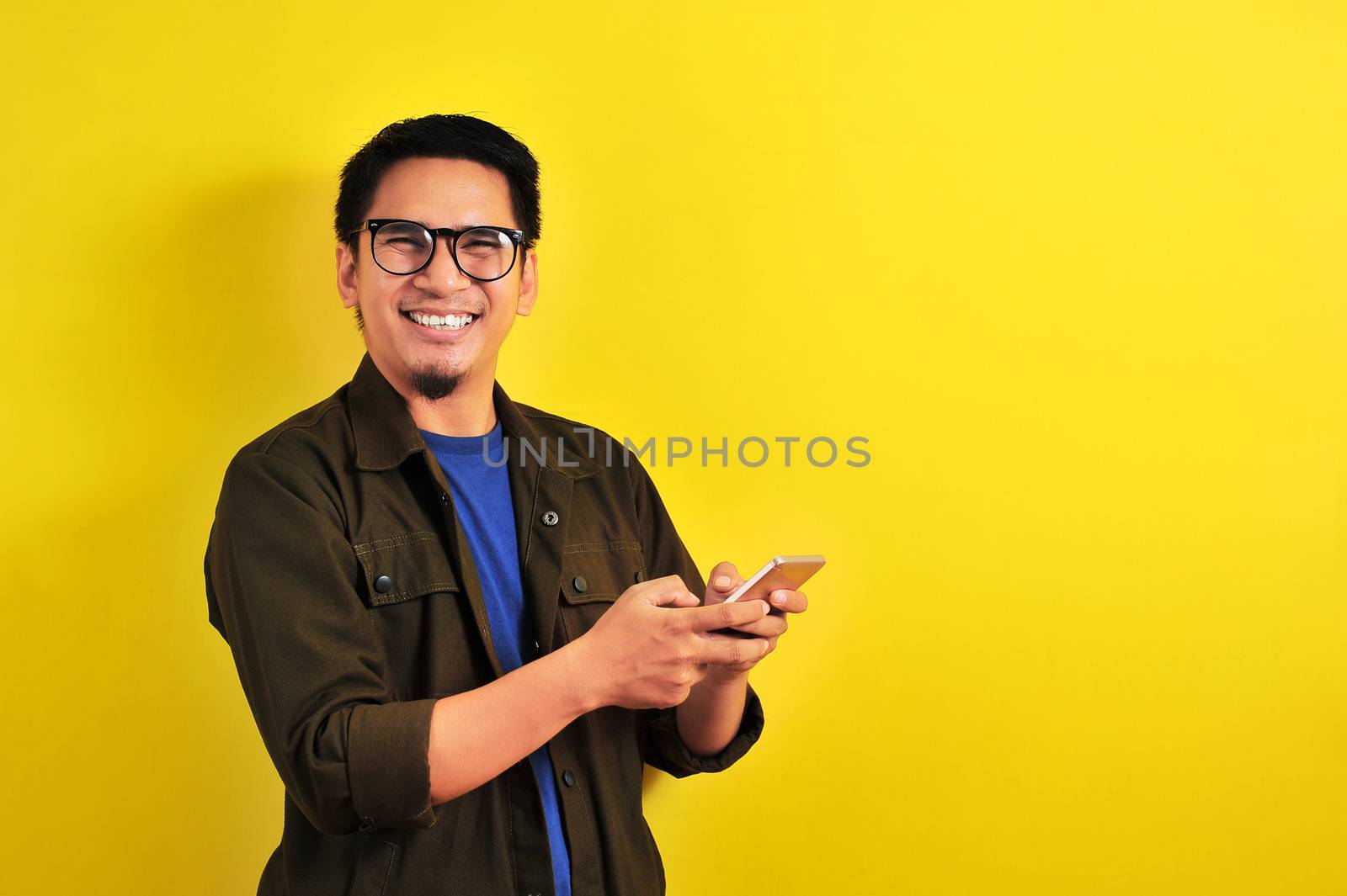 Portrait of happy smiling Asian man using smartphone wearing casual t-shirt and jacket with eyesglasses, get the best price, using simple mobile banking payment