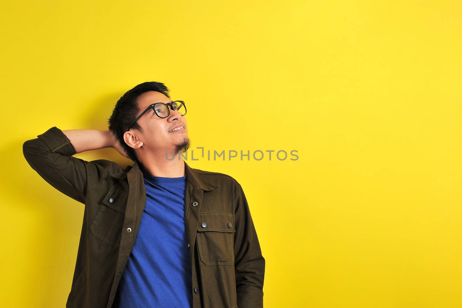 Asian man wearing glasses smiling look at copy space, isolated on yellow background