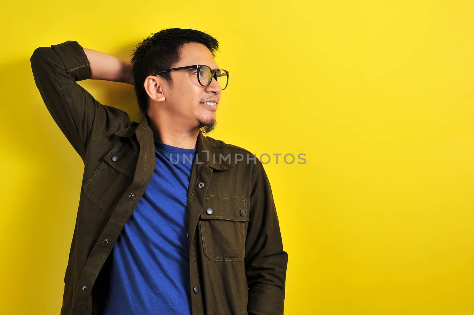 Asian man wearing glasses smiling look at copy, isolated on yellow background