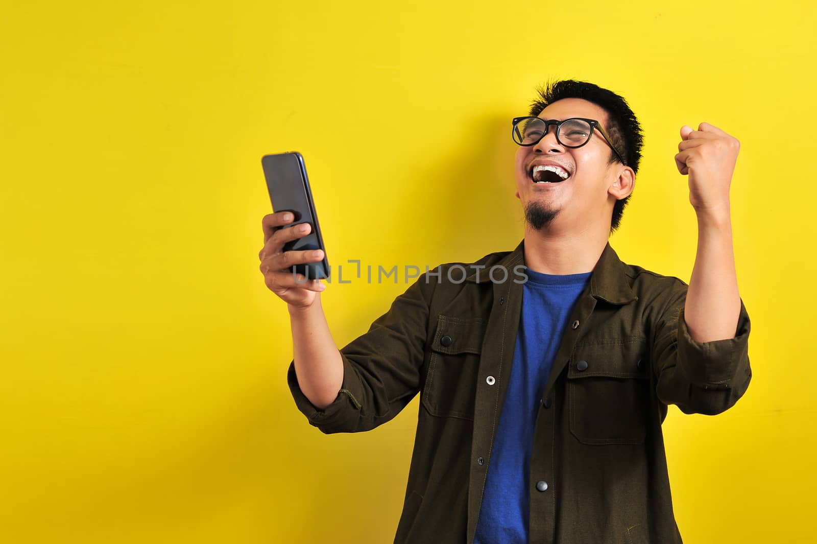 Asian man holding smartphone with winning gesture by heruan1507
